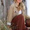abbey-saunders-17 A smiling blonde woman sits outdoors against a rustic wooden wall, wearing casual neutral autumn clothing.
