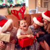 Family Wearing Santa Hats Sitting On Sofa At Home Opening Christmas Gifts