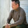 A mature man in a bright yellow floral shirt sits relaxed on a rustic wooden deck outdoors.