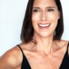 A smiling brunette woman with a friendly, relatable expression, posing against a clean, neutral white background.