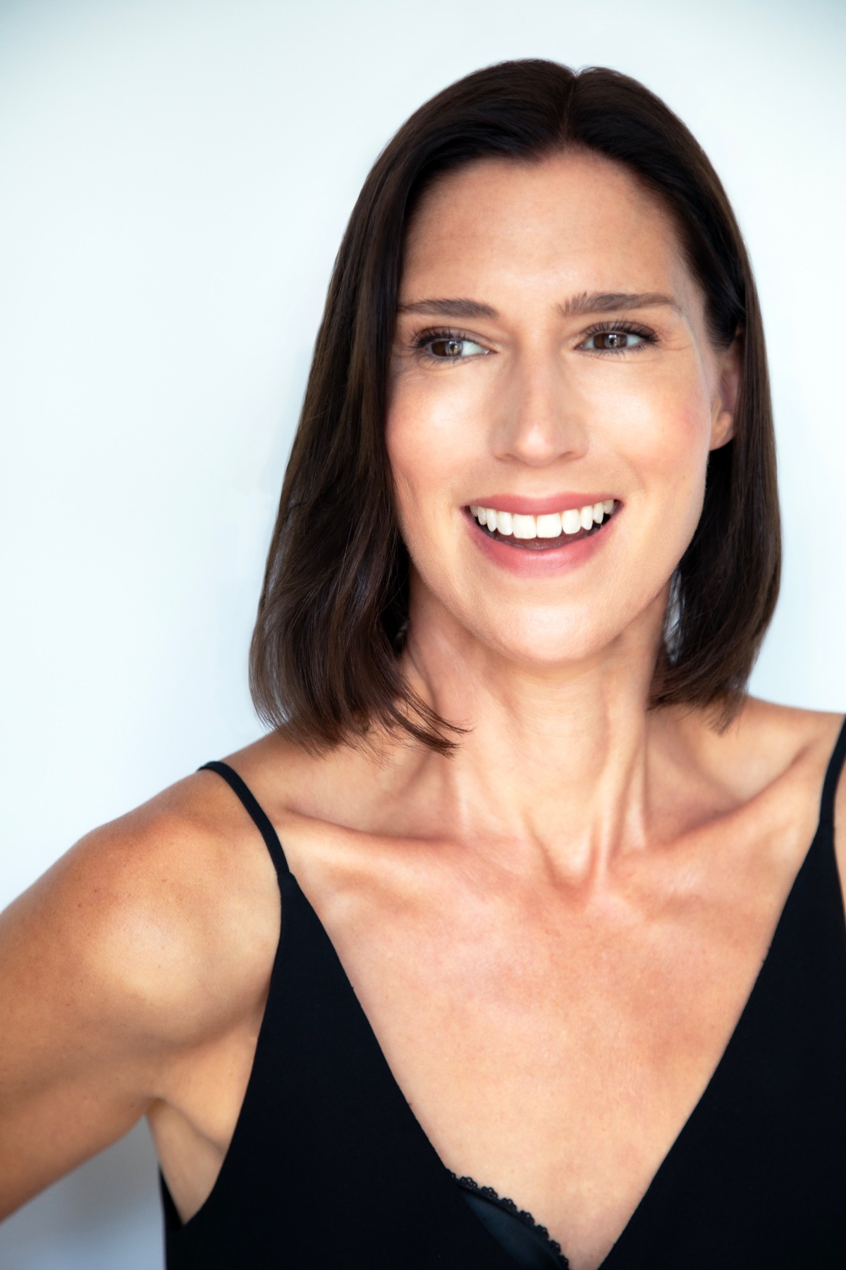 A smiling brunette woman with a friendly, relatable expression, posing against a clean, neutral white background.