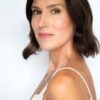A dark-haired female model with a natural and polished look, posing against a clean white backdrop.