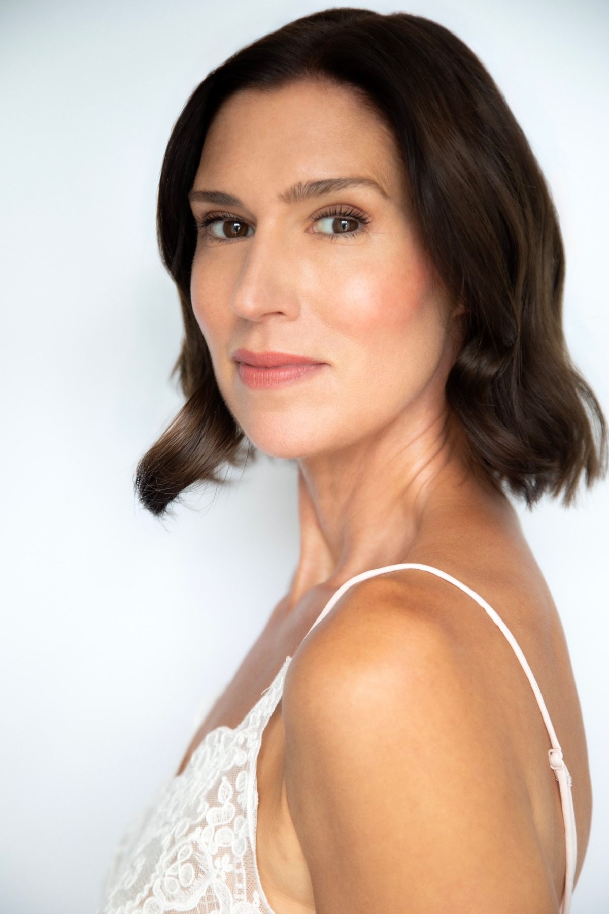 A dark-haired female model with a natural and polished look, posing against a clean white backdrop.