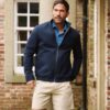 A mature man in a navy jacket and beige shorts standing outdoors in a garden setting.