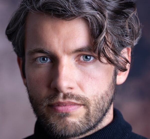 A man with blue eyes and salt and pepper hair looking directly into the camera lens indoors.