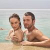 A man and woman relaxing together in a calm infinity pool on a sunny vacation day.