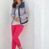 A smiling mature woman in a colourful tweed jacket and pink trousers leans against a white wall.