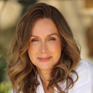 A radiant woman wears a white linen shirt and jeans while posing naturally in a sunny garden setting