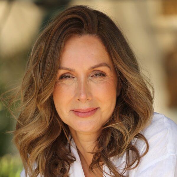 A radiant woman wears a white linen shirt and jeans while posing naturally in a sunny garden setting