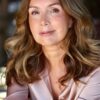 Mature woman with a warm, friendly smile looks directly into the camera in a soft natural light portrait.