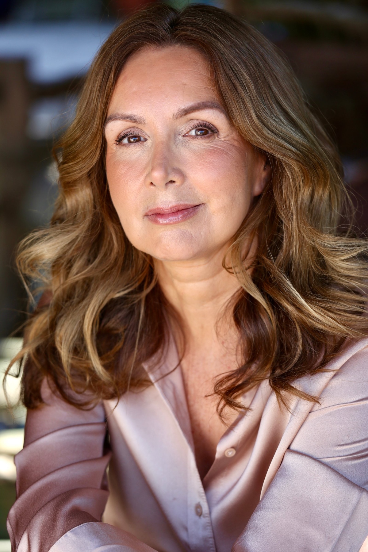 Mature woman with a warm, friendly smile looks directly into the camera in a soft natural light portrait.