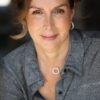 Mature woman with a warm, friendly smile looks directly into the camera in a soft natural light portrait.
