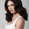 A dark-haired female model poses for a clean professional headshot against a neutral grey studio background.
