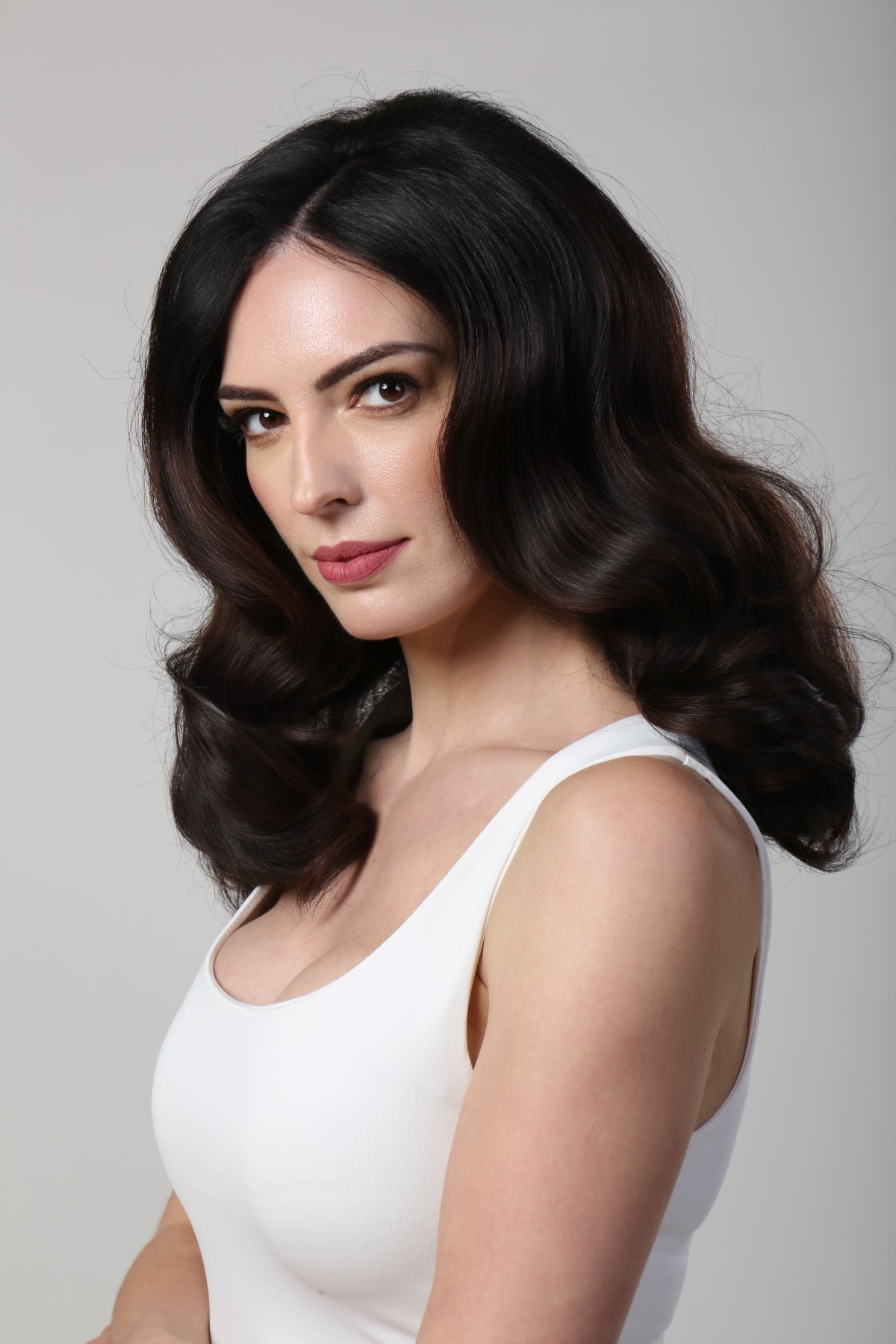 A dark-haired female model poses for a clean professional headshot against a neutral grey studio background.