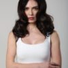 A brunette woman with wavy hair wears a white tank top against a neutral studio background.