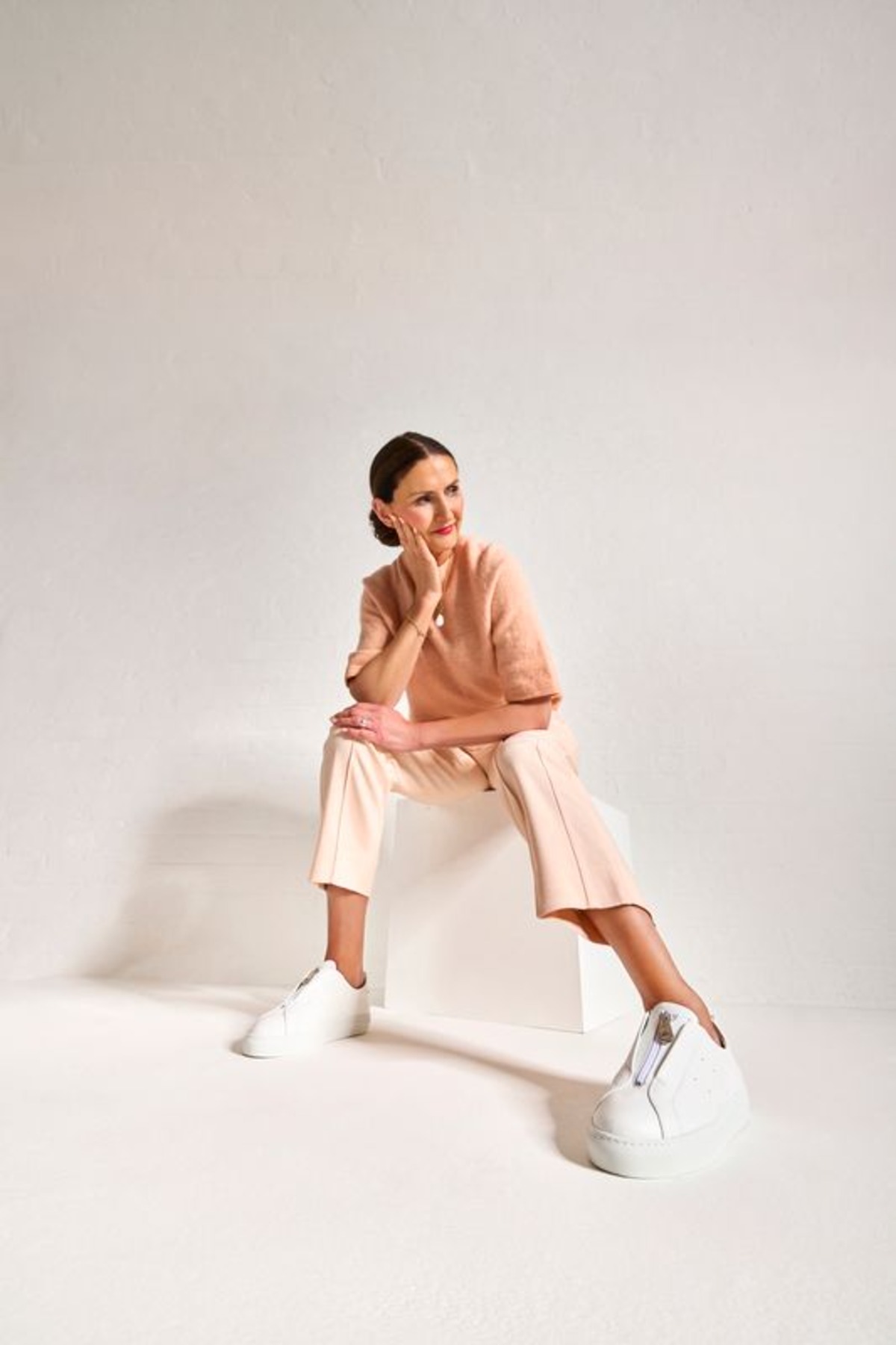 A smiling mature woman in a polished white suit stands against a neutral backdrop for commercial brand photography.