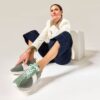 A mature woman sits in a bright studio, wearing stylish casual attire and green platform fashion sneakers.