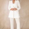 A smiling mature woman in a polished white suit stands against a neutral backdrop for commercial brand photography.
