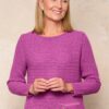 vanessa-crookes-15 A smiling mature woman with blonde hair wears a vibrant purple sweater against a neutral textured background.