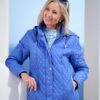 vanessa-crookes-16 A cheerful mature woman in a blue quilted jacket smiles while standing outdoors in bright daylight.