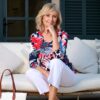 vanessa-crookes-22 A mature blonde woman sits gracefully on a white outdoor sofa, exuding a warm and professional demeanor.