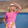 vanessa-crookes-25 A smiling mature woman in a pink shirt and sun hat enjoys a bright sunny day outdoors.