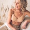 vanessa-crookes-39 A radiant middle-aged woman wearing a neutral bra laughs naturally while sitting in a sunlit bright room.