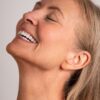 vanessa-crookes-40 A radiant middle-aged woman with blonde hair laughing with her head tilted back against a neutral background.