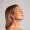 vanessa-crookes-41 A mature woman with natural grey-blonde hair rests peacefully with her eyes closed against a neutral backdrop.