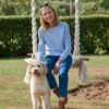 vanessa-crookes-5 A smiling blonde woman wearing a blue jumper sits on a garden swing beside her happy dog.