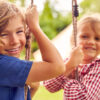 Portrait Of Two Children Playing On Swing In Garden At Home