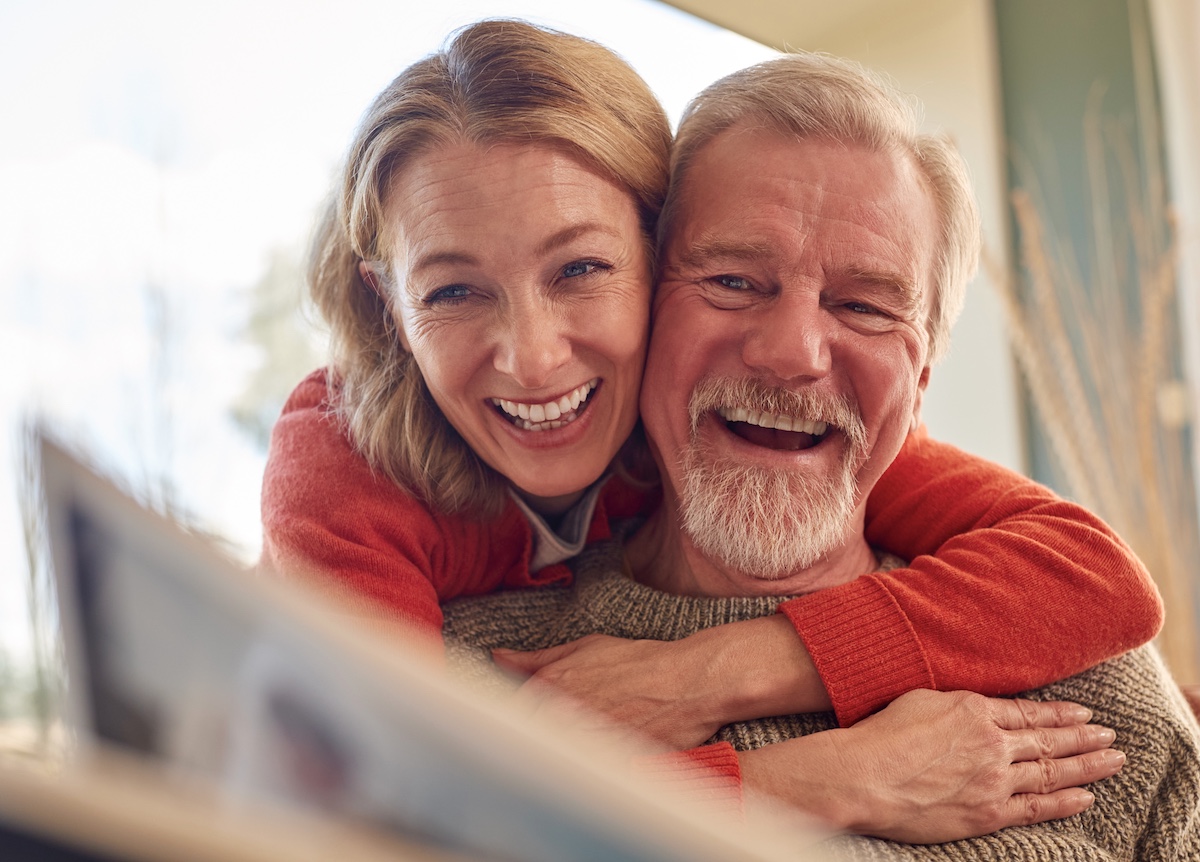 Smiling Senior Couple At Home Enjoying Looking Through Photo Album Together