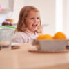Smiling Young Girl Wearing Pyjamas Sitting At Table In Kitchen At Home Waiting For Breakfast