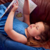 Close Up Of Father And Daughter Lying On Sofa At Home As Girl Reads Book