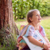 Smiling Young Girl Sitting Under Tree In Garden Reading Story Book