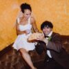 A joyful bride and groom playfully sharing a plate of fries and sauce inside a cozy venue.