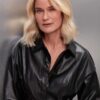Mature blonde female model with a neutral expression wearing a black leather shirt against metallic background.