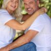 A happy middle-aged couple in white t-shirts and jeans smiling warmly while embracing in a garden setting.