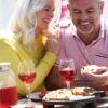 A happy mature couple shares pizza and drinks together at a sunlit outdoor table, radiating authentic warmth.