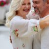 A happy mature couple share a warm embrace, smiling brightly while wearing casual white spring clothing outdoors.