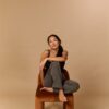 trinh-nguyen-11 A smiling woman sits cross-legged on a velvet chair against a warm, neutral studio backdrop background.