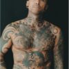 A bald, heavily tattooed man with body art pose against a simple black background for a portrait.