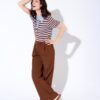 A smiling woman in a striped polo and brown trousers poses against a bright white studio background.