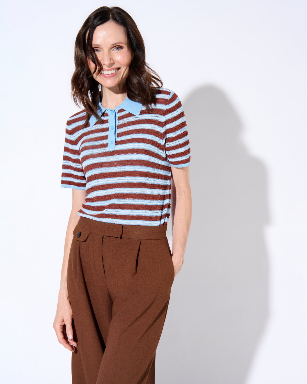 sasha-finn-13 A smiling woman with dark hair wears a striped polo shirt while posing against a white background.