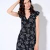 A brunette woman wearing a black floral dress poses against a clean white studio background for work.