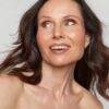 A close up beauty shot of a mature woman with dark hair smiling and looking to the side.