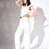 A woman with wavy brown hair poses in a bright white studio wearing elegant white summer clothing.