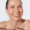 A radiant middle-aged woman with natural skin texture smiles brightly in a clean, high-key studio setting.