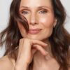 A smiling brunette woman with natural makeup poses for a bright and professional commercial headshot against grey.