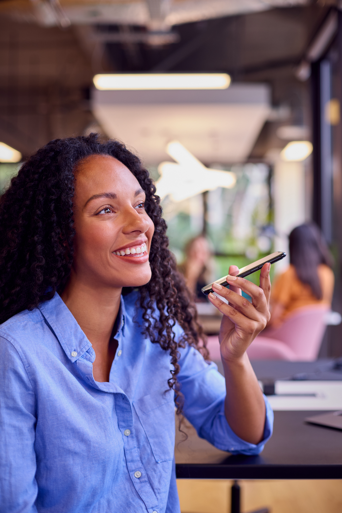 Businesswoman Sitting At Desk In Office Talking Into Mic Of Mobile Phone